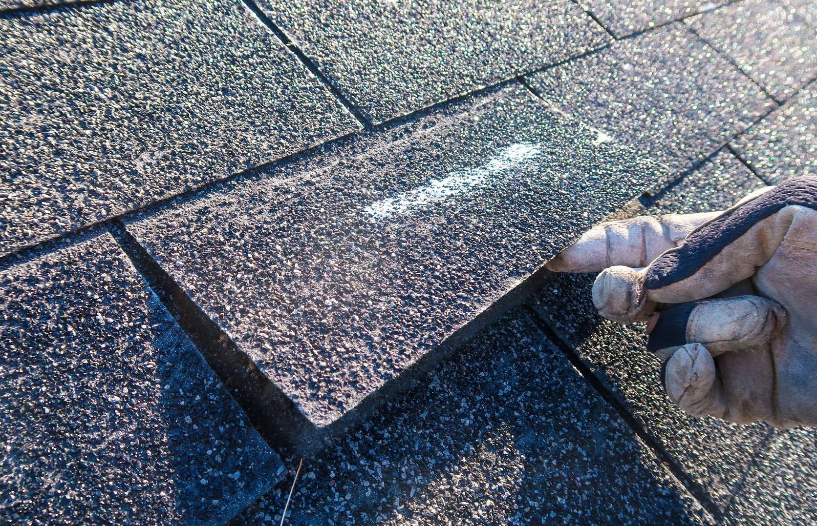 A person is holding a piece of shingles on a roof.