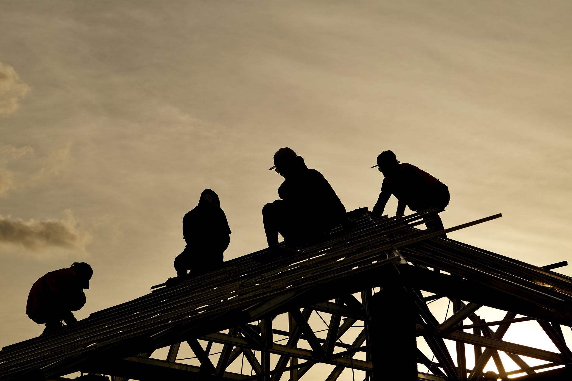 A group of construction workers are silhouetted against a cloudy sky.