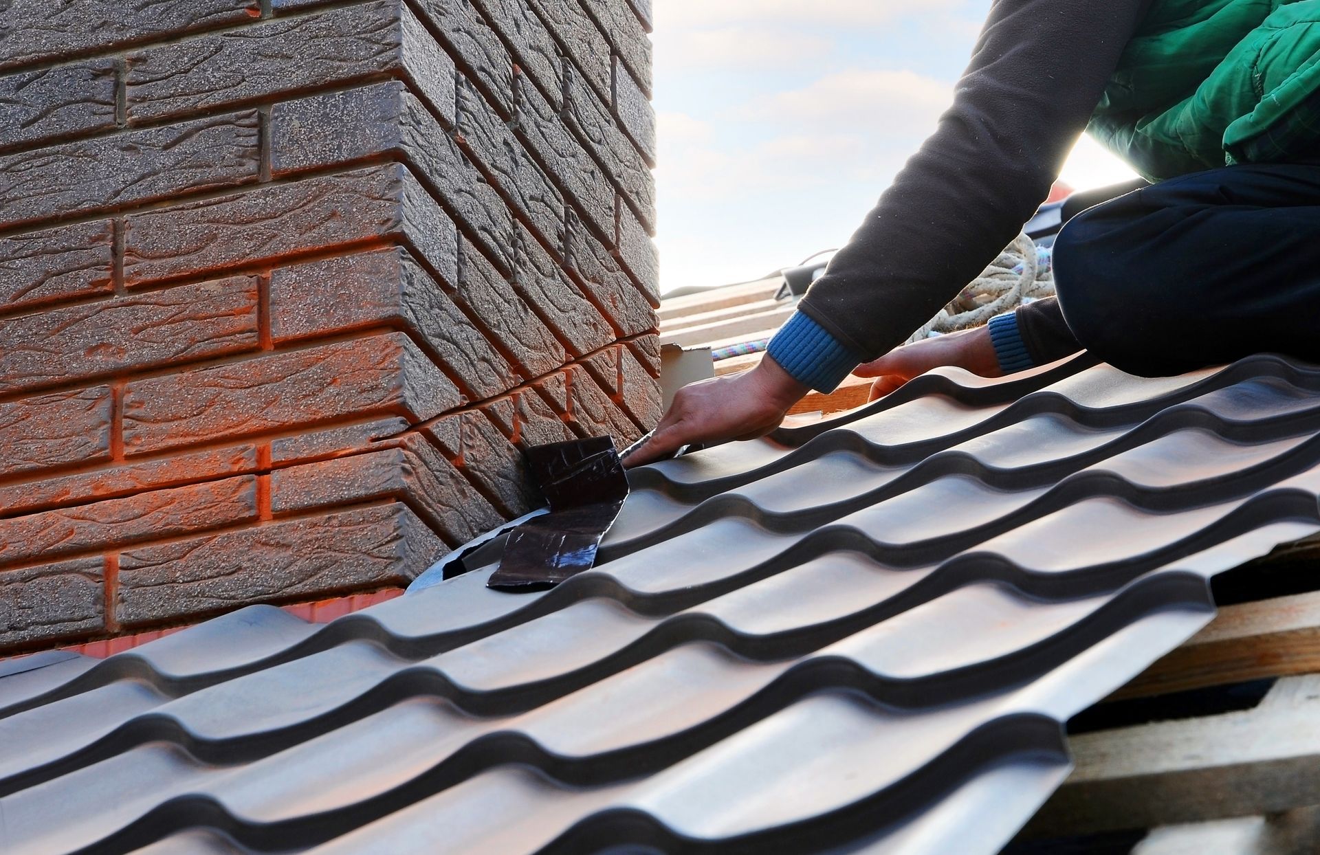 A man is working on a roof with a chimney in the background.