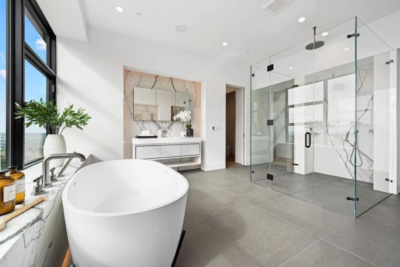 Modern bathroom with a freestanding tub, glass shower, and large windows.
