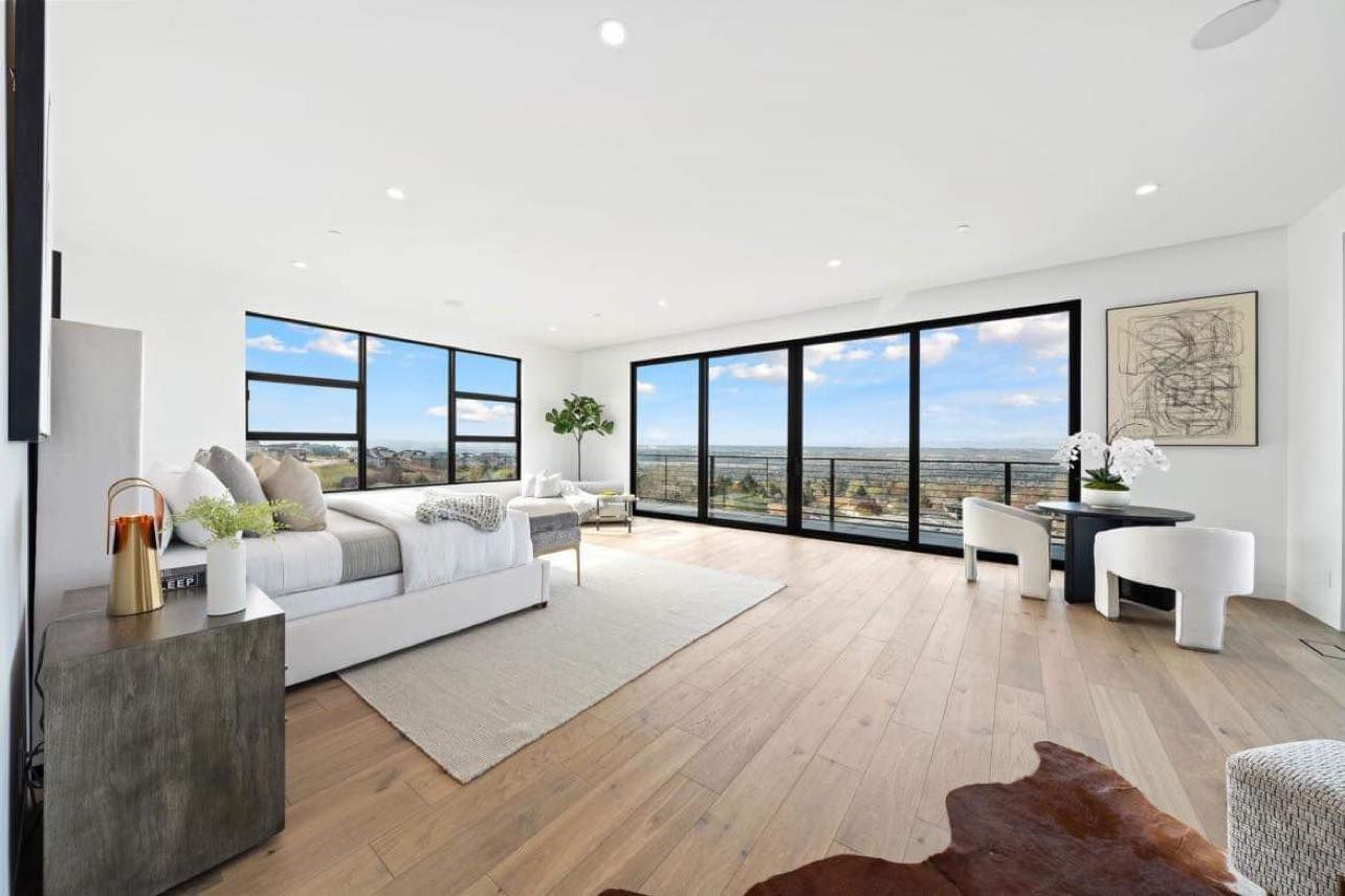 Bright, modern living room with large windows overlooking a city and a light wood floor.
