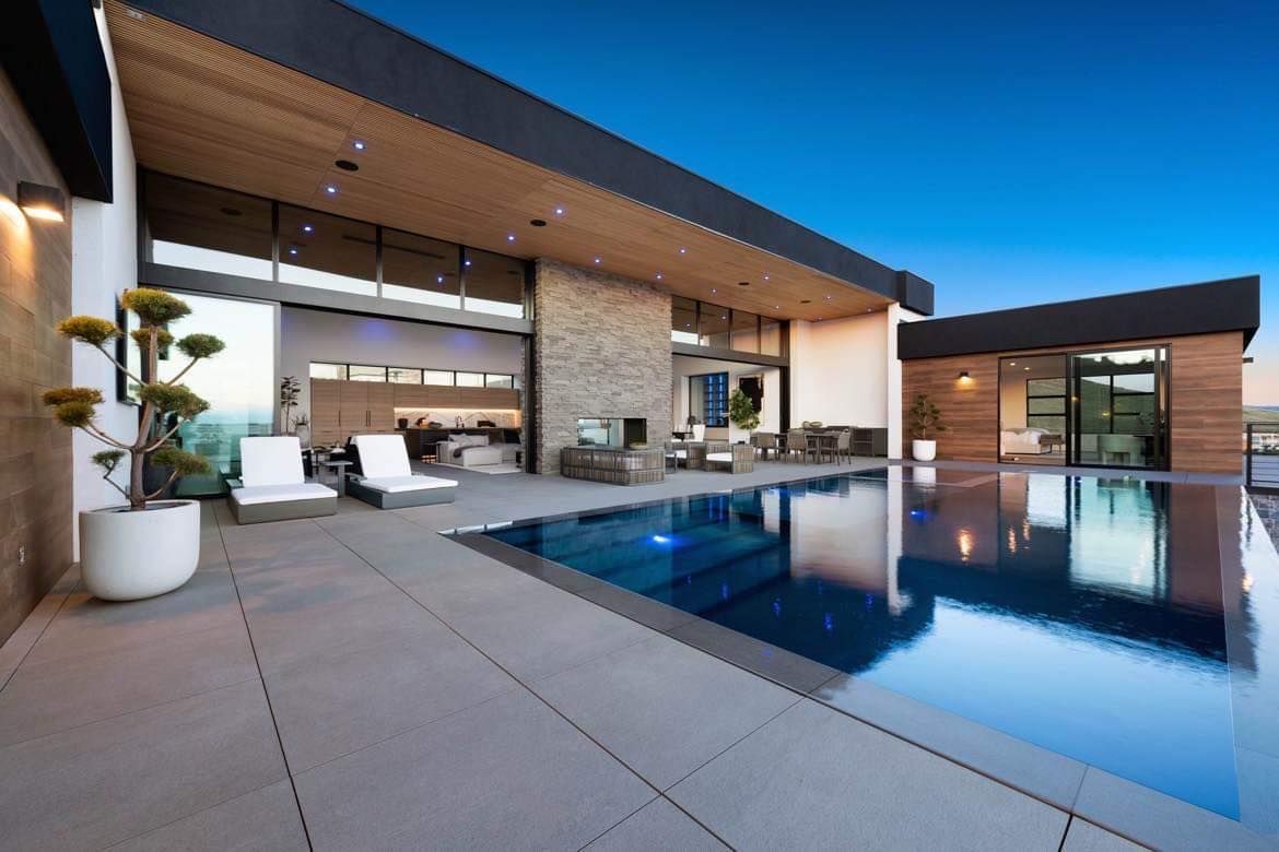 Modern home exterior with pool. Blue water, patio with lounge chairs.