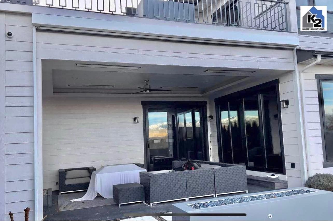 Outdoor patio with seating, ceiling fan, and black framed doors, with mountain views reflecting.