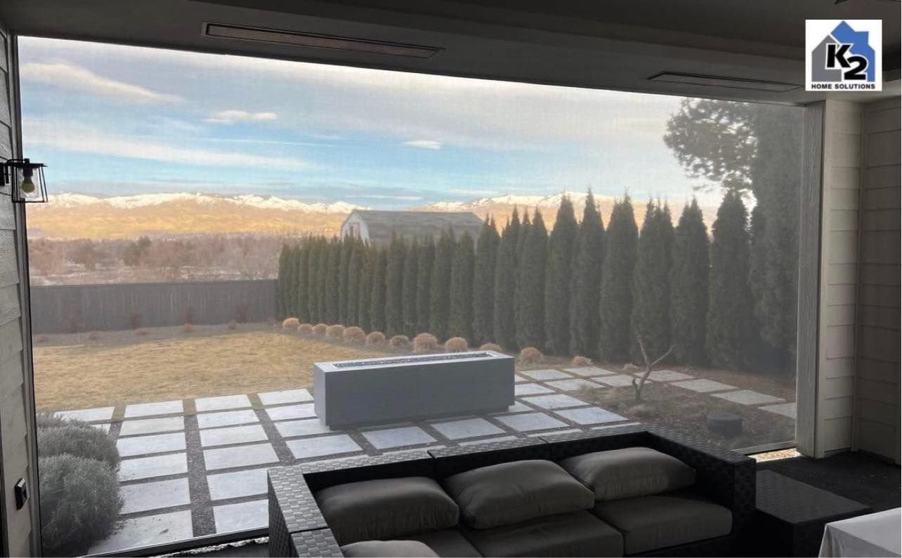 Outdoor living space with retractable screen overlooking a landscape.  Gray patio furniture, fire pit, and trees are visible.