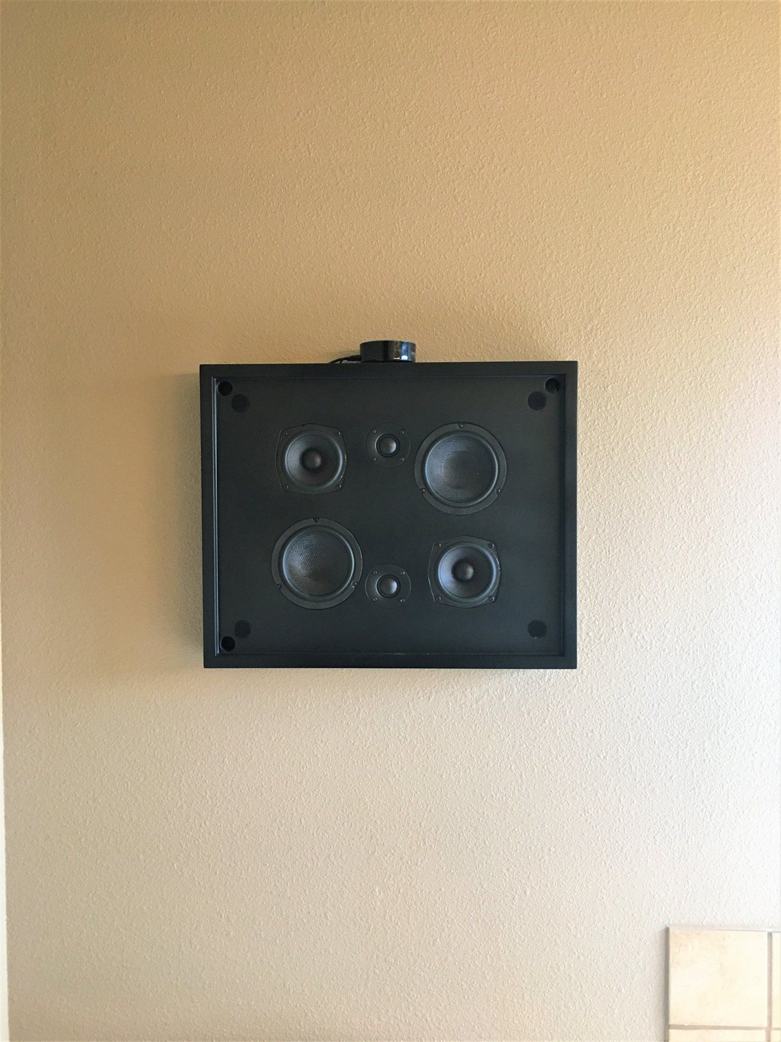 Black speaker system mounted on a beige, textured wall.