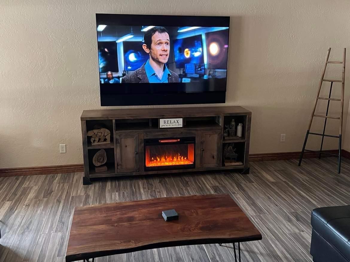 Living room with large TV over fireplace, wooden coffee table, and wood-look flooring.