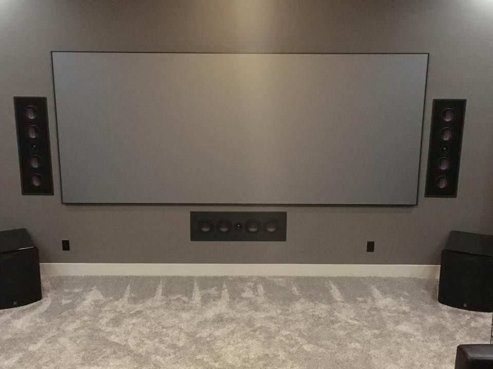 Home theater with gray screen, speakers, and plush carpet on a gray wall.