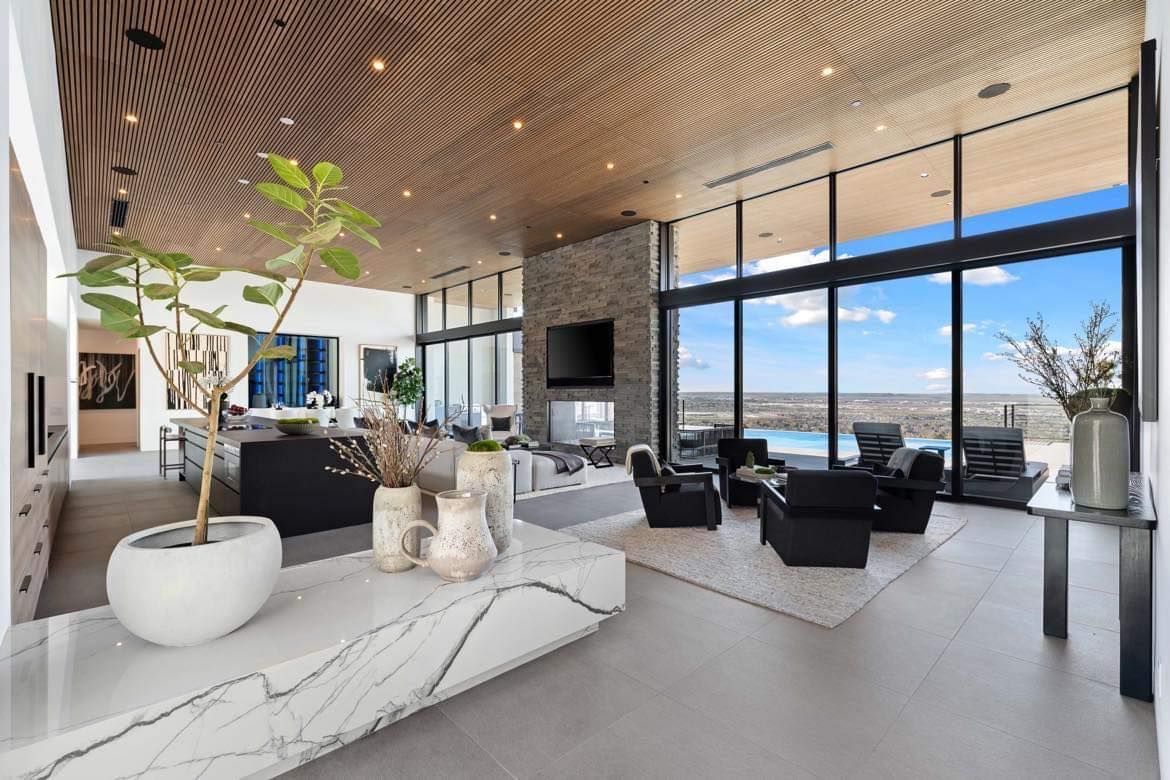 Spacious living room with floor-to-ceiling windows, stone fireplace, and marble accents overlooking a scenic view.