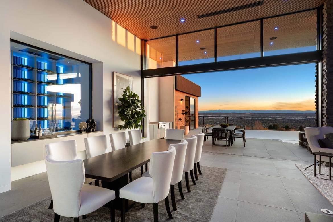 Luxurious dining room with long table, white chairs, and expansive view through open doors.