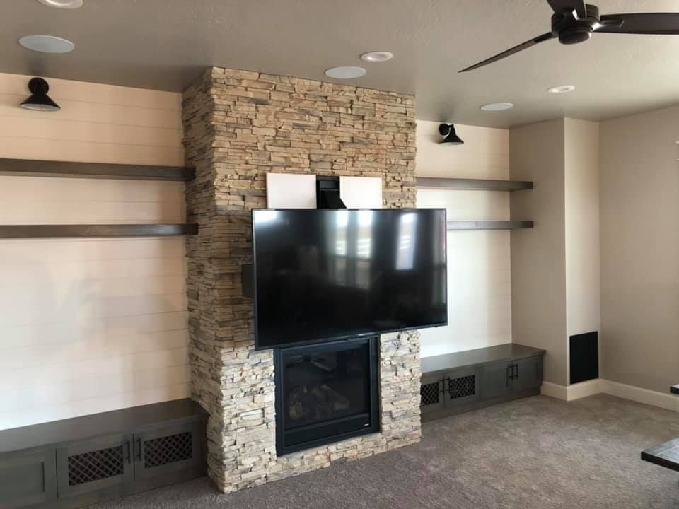 Stone fireplace with mounted TV, built-in storage, floating shelves, and speakers in a living room.