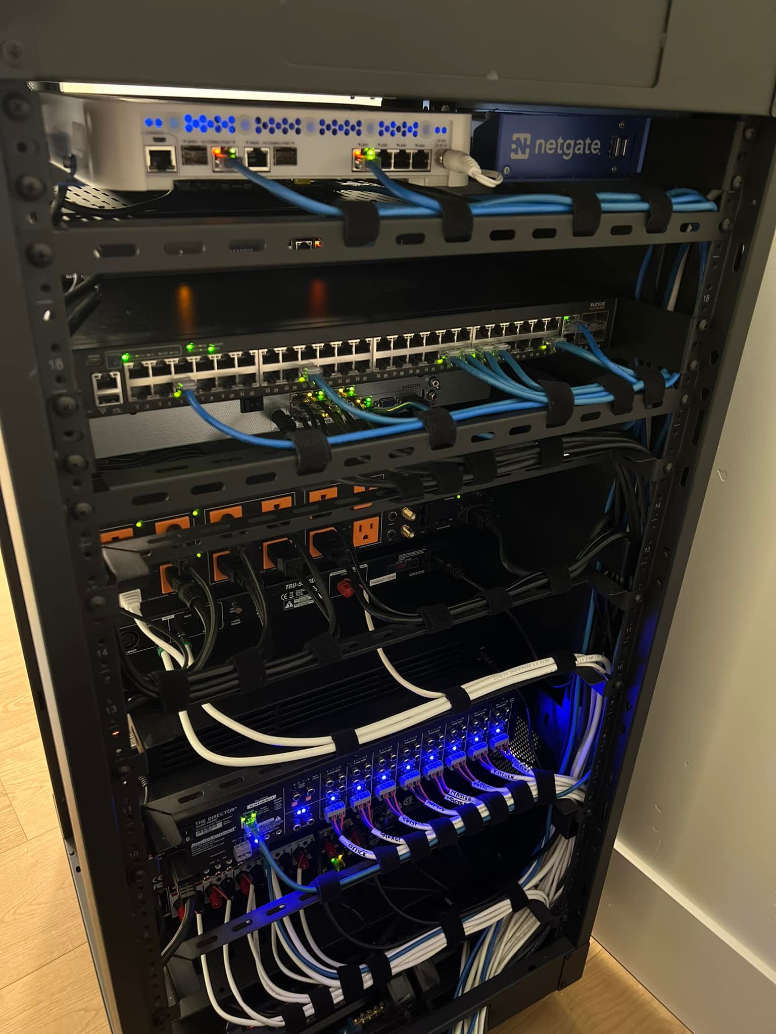 Black server rack with network equipment: router, switch, patch panels, and cabling.