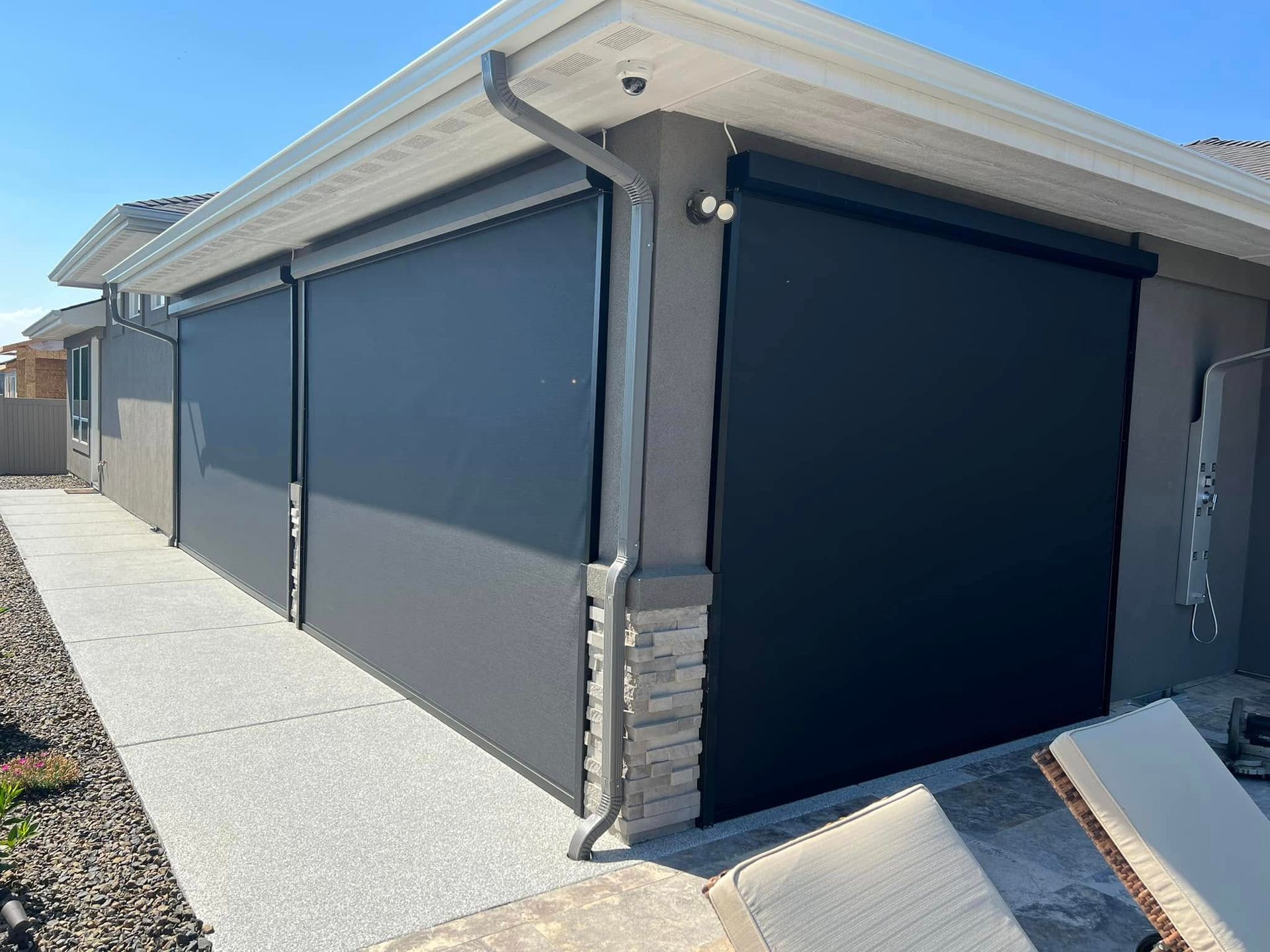 Exterior of a home with retractable black shades on a patio, gray concrete, and a downspout.