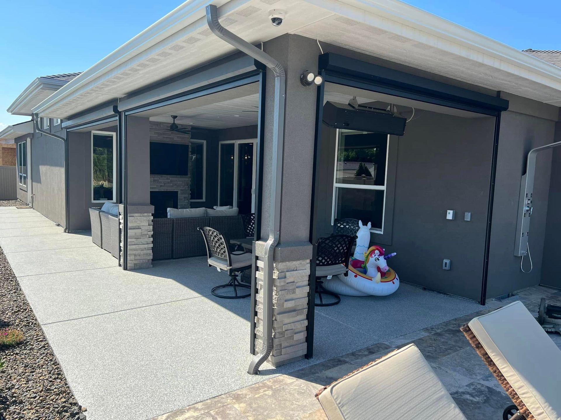 Outdoor patio with a concrete floor and grey stucco walls, featuring roll-down shades and a pool float.