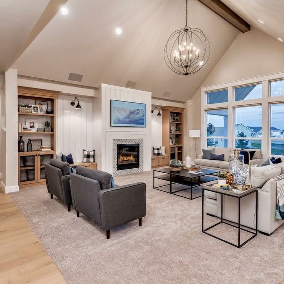 Spacious living room with fireplace, built-in shelving, gray furniture, large windows, and a modern chandelier.