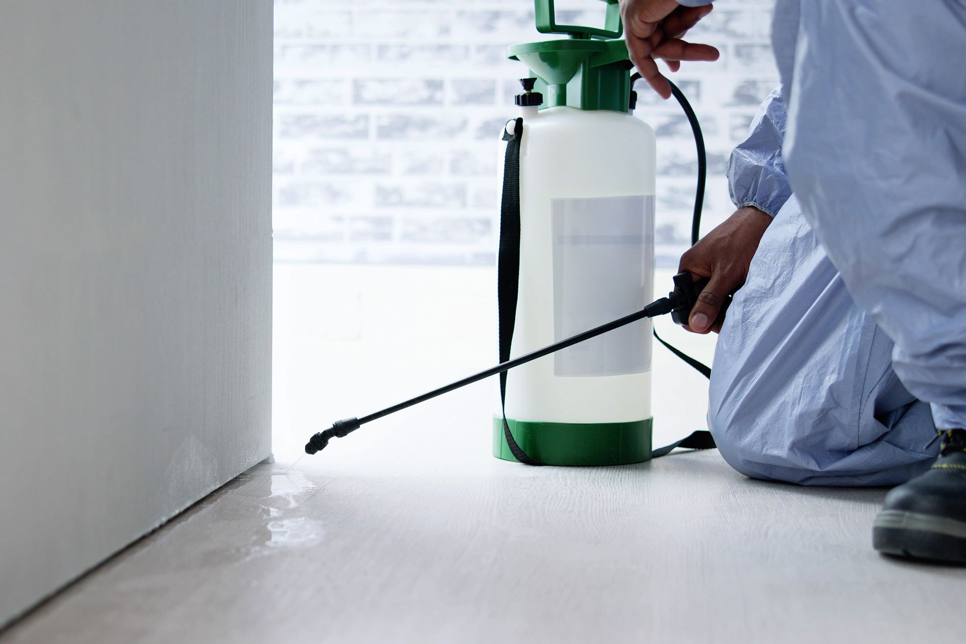 Pest control worker in blue suit spraying insecticide on floor.