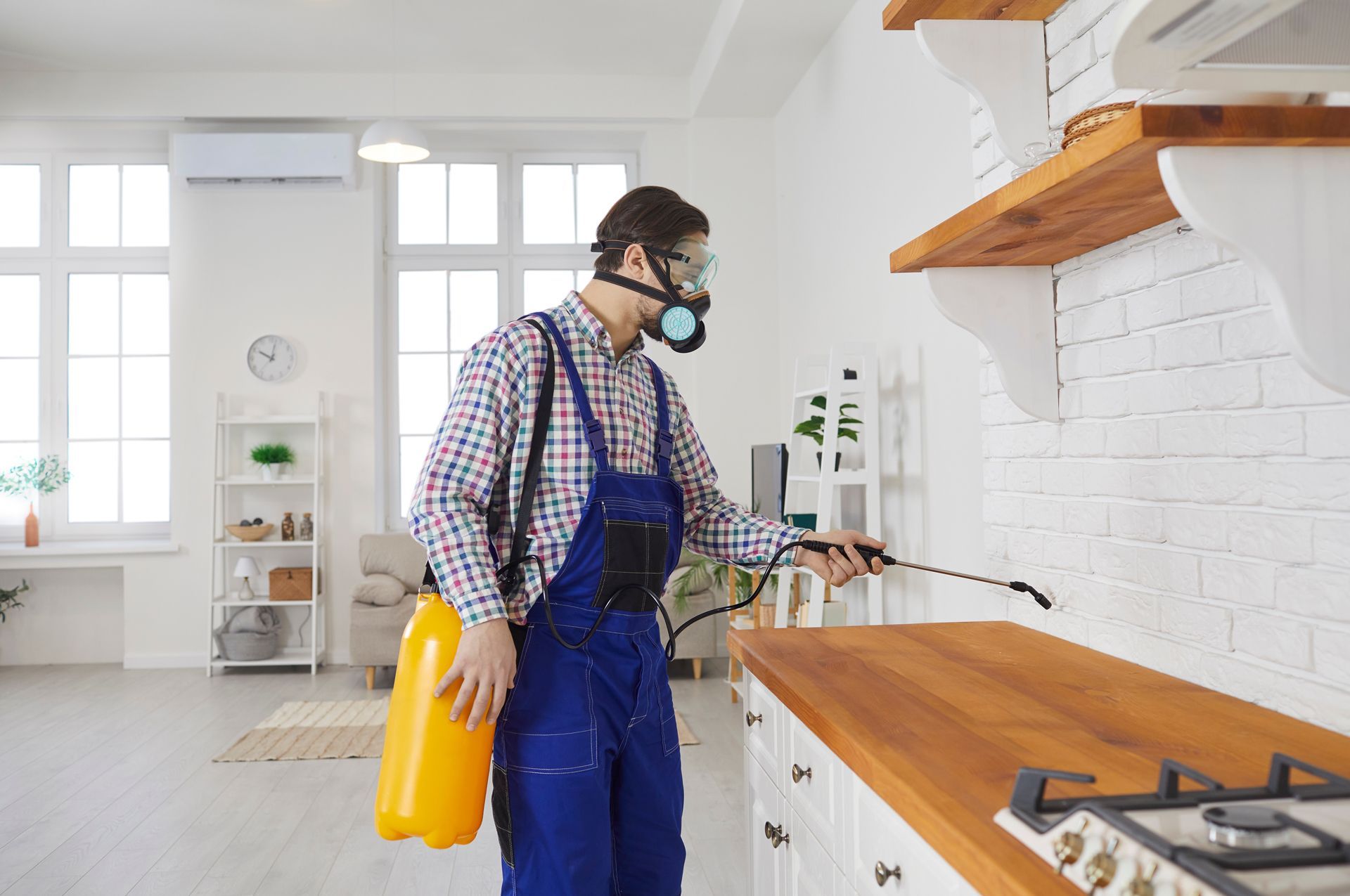 A Man Wearing a Gas Mask is Spraying a Kitchen Counter With a Sprayer