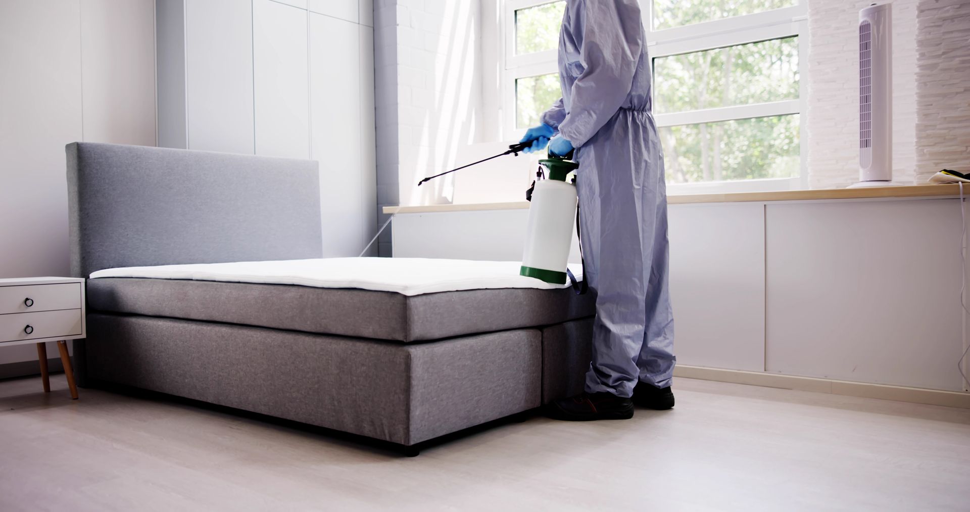 A Man in a Protective Suit is Spraying a Mattress in a Bedroom