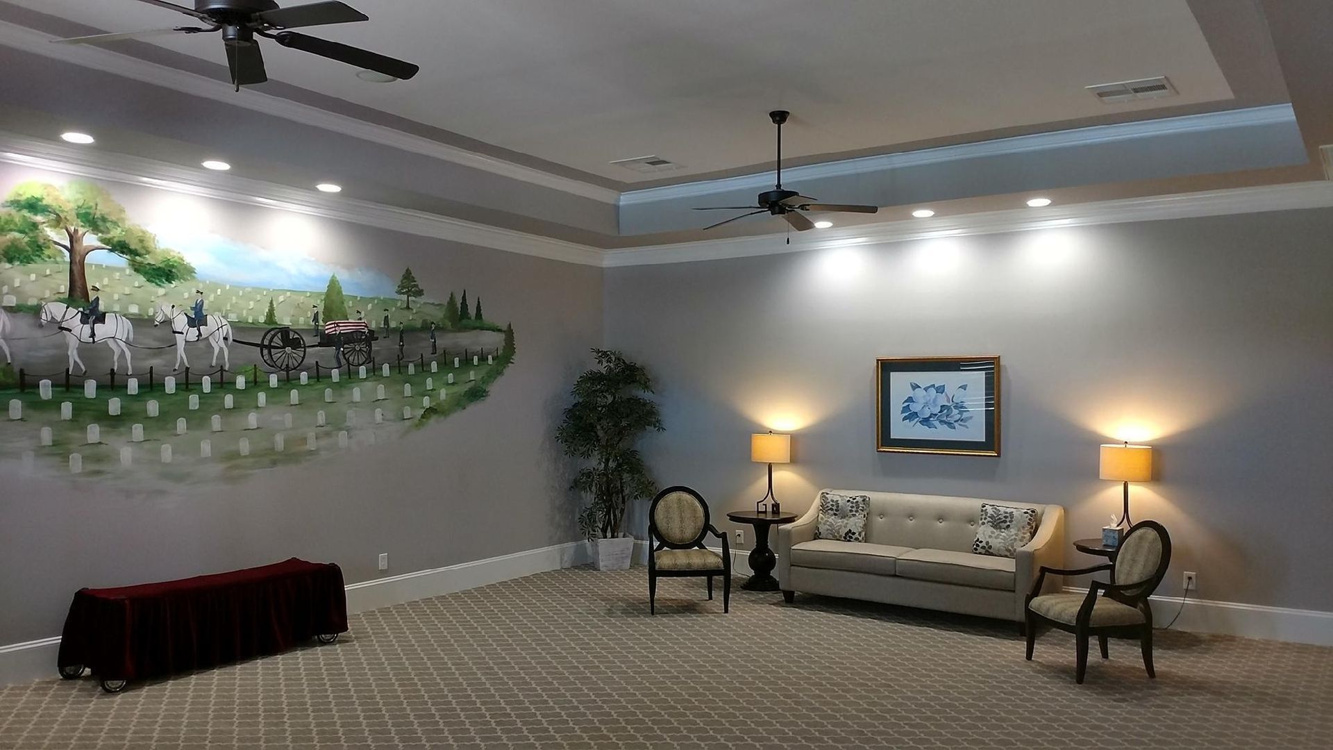 A memorial room with a mural, seating, and a casket. Warm lighting and neutral colors create a somber atmosphere.