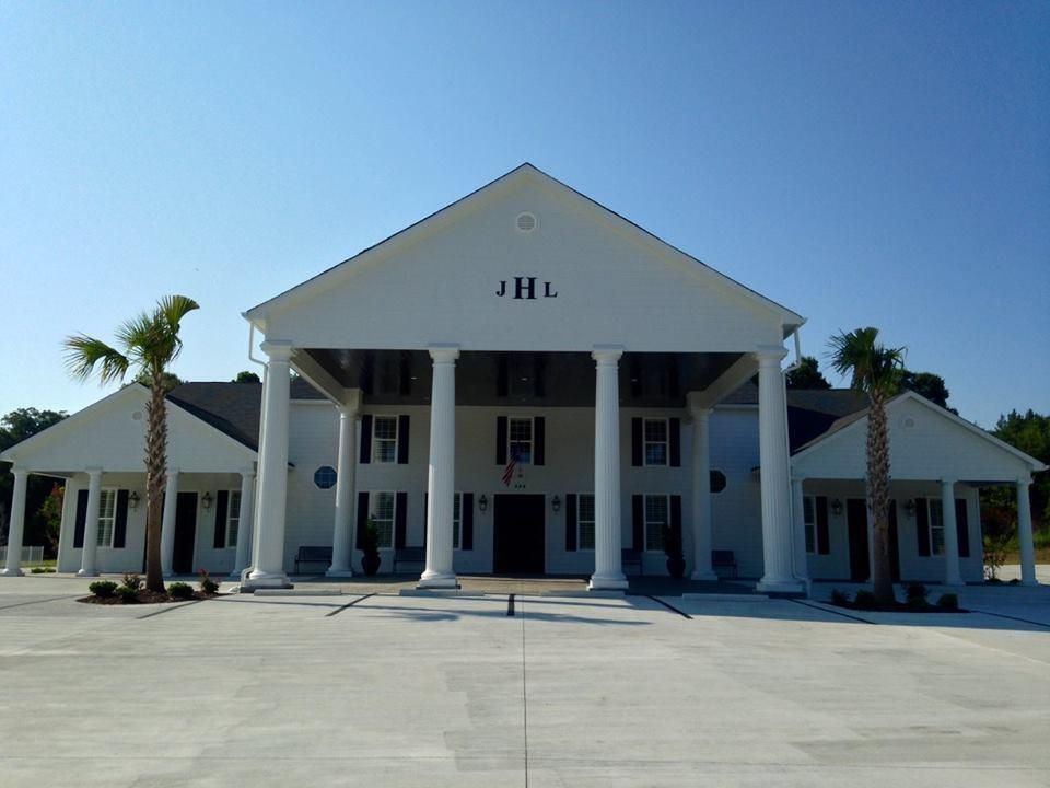 White building with columns, palm trees; bright blue sky.