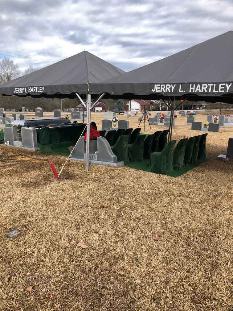 Funeral service setup at a cemetery with tents, chairs, and a headstone.