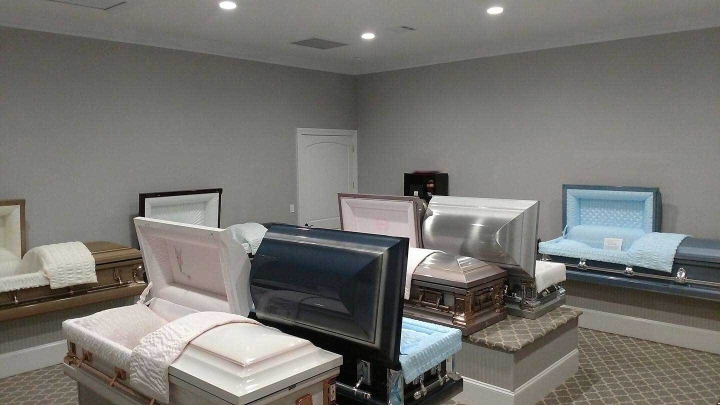 A funeral home showroom with various open caskets in different colors displayed on pedestals.
