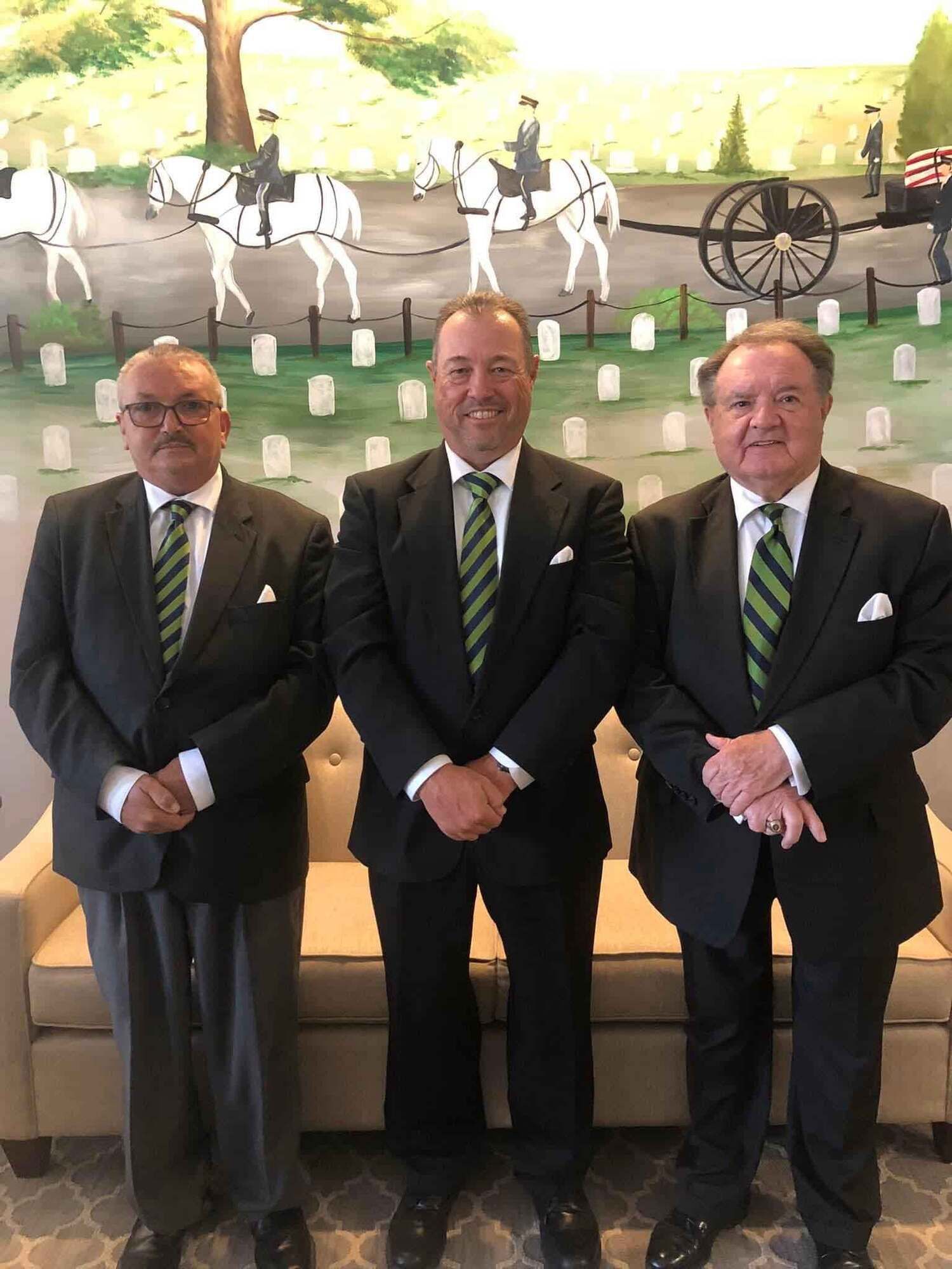 Three men in suits stand in front of a mural.