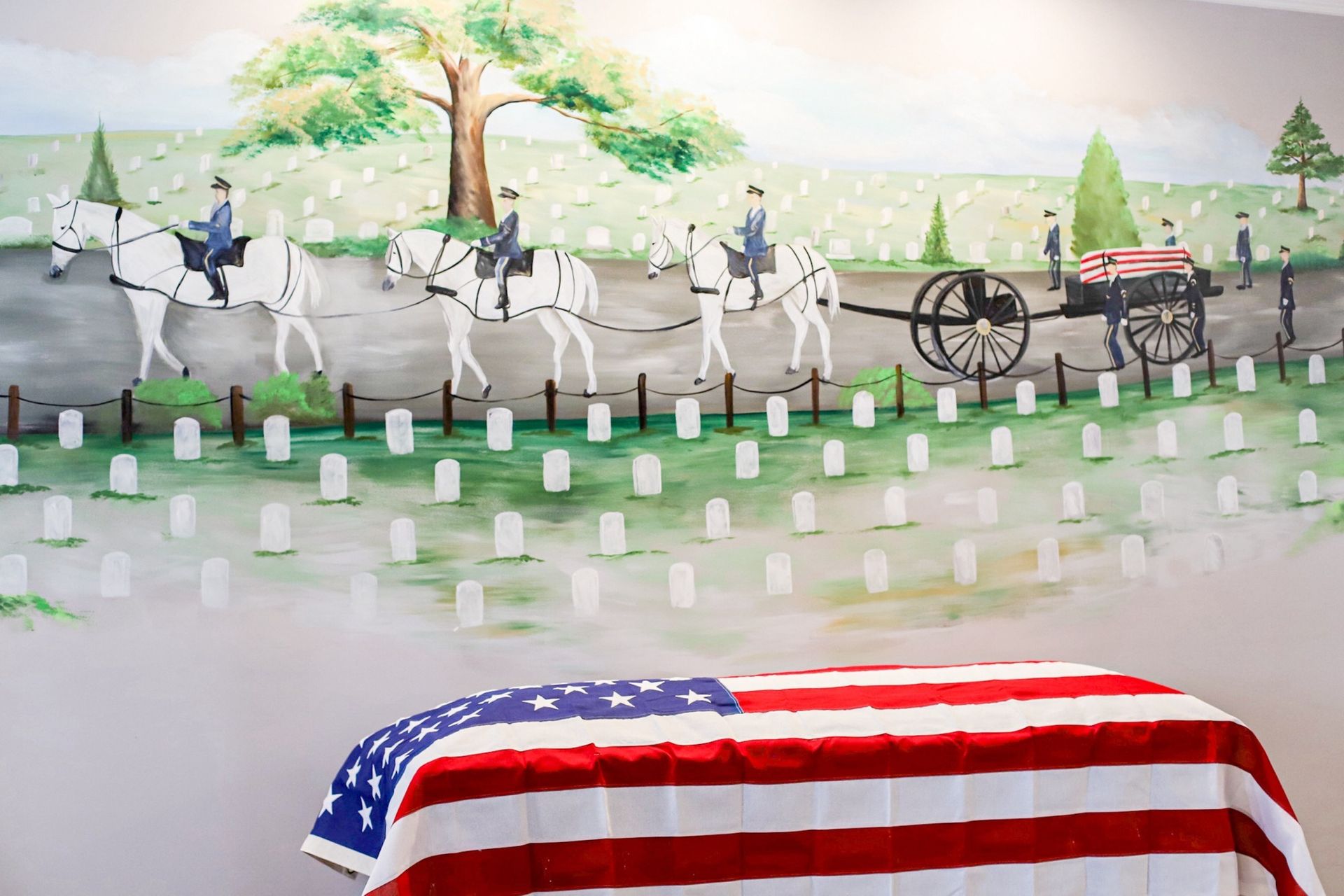 A coffin draped in an American flag sits below a mural of a funeral procession with white horses and soldiers.