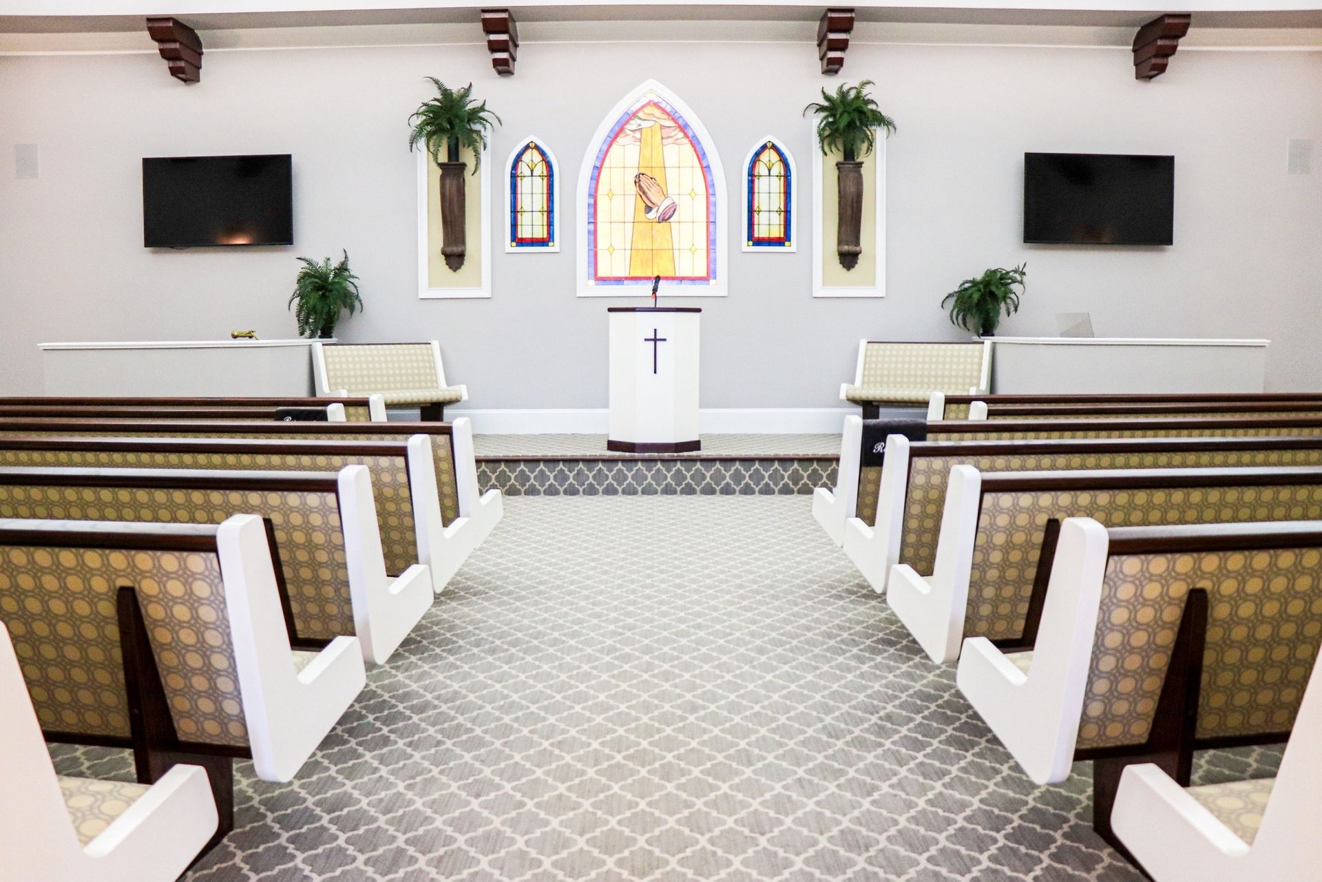 Interior of a chapel with pews, pulpit, and a stained glass-like focal point with a cross.
