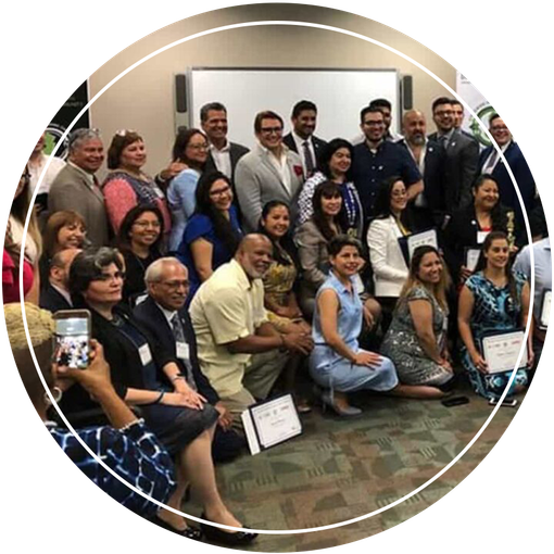 Group of diverse people pose together in a room, many holding certificates.  A whiteboard is in the background.