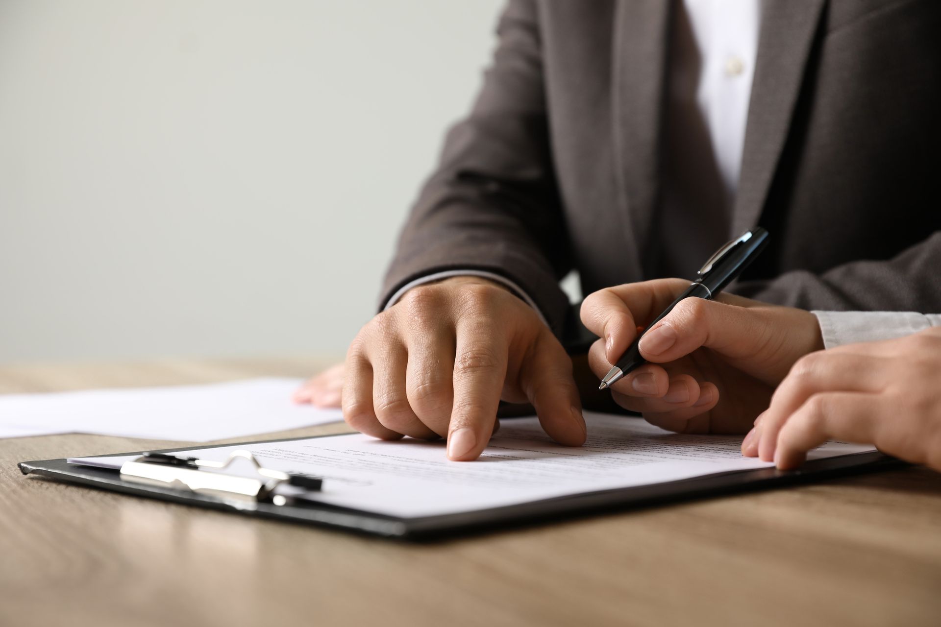 Two people at a table, one pointing at document on clipboard, the other holding a pen.