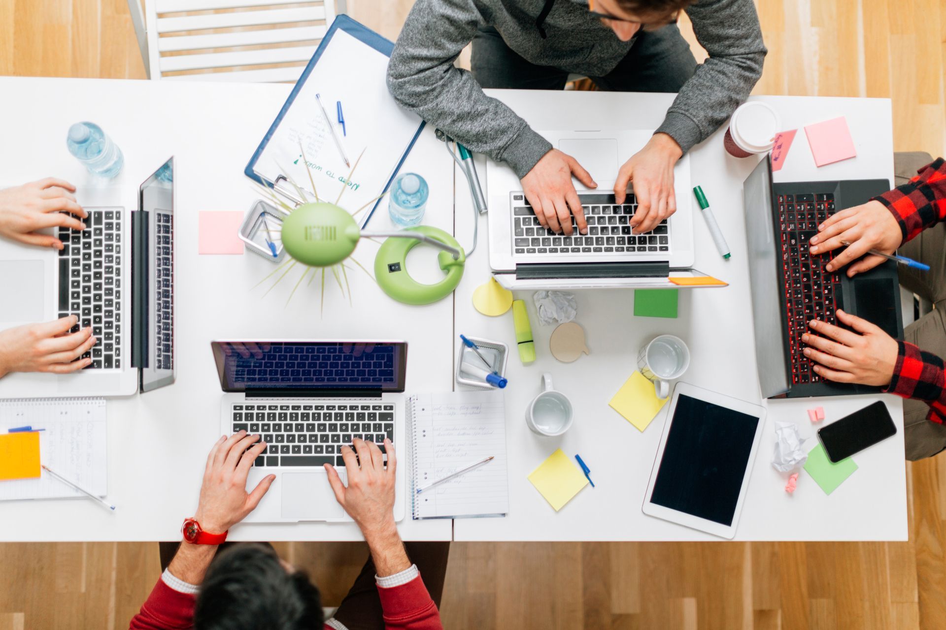 Overhead view of a team working at a white table with laptops, papers, and office supplies.