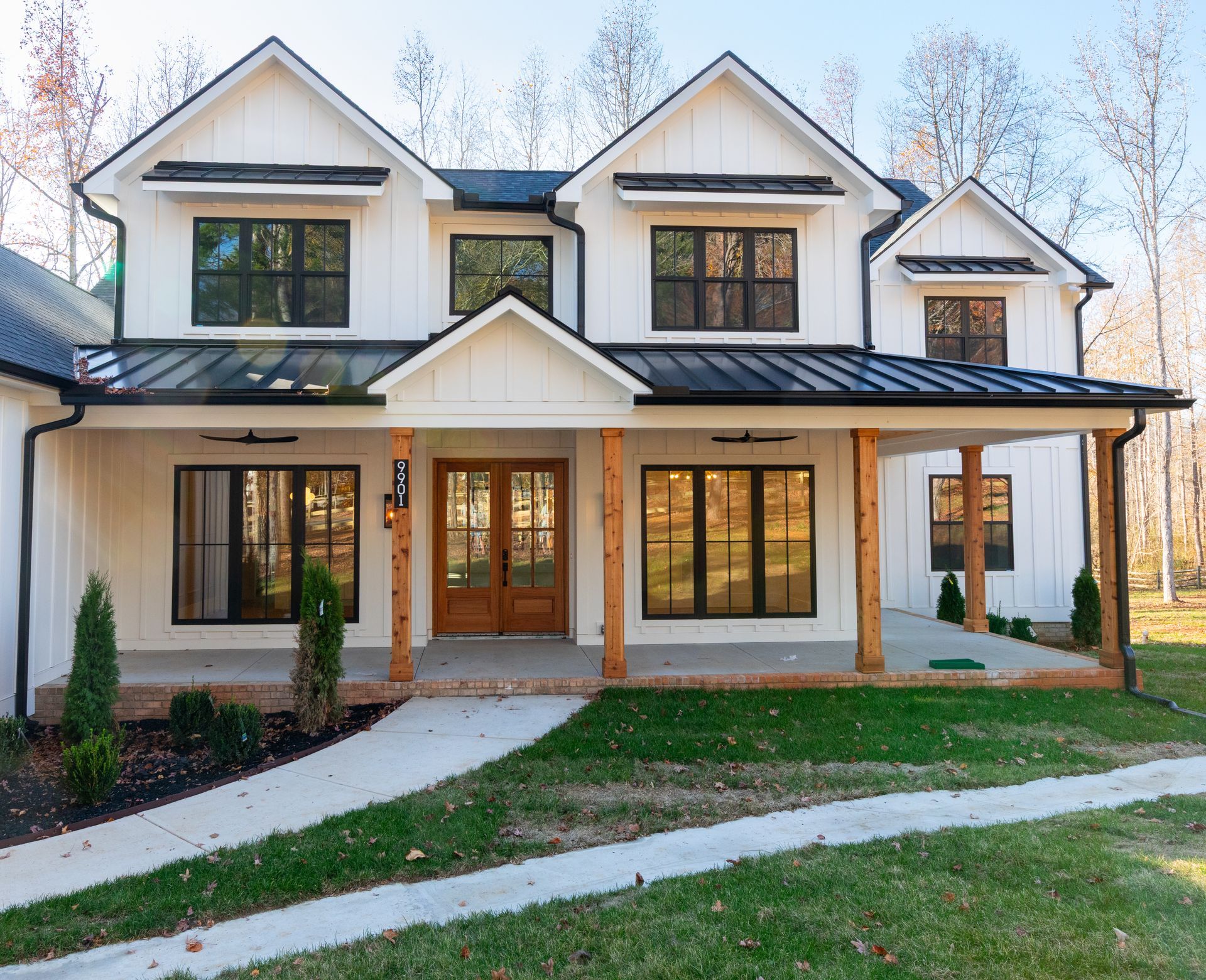 White farmhouse with black trim, a porch, and a brown front door.