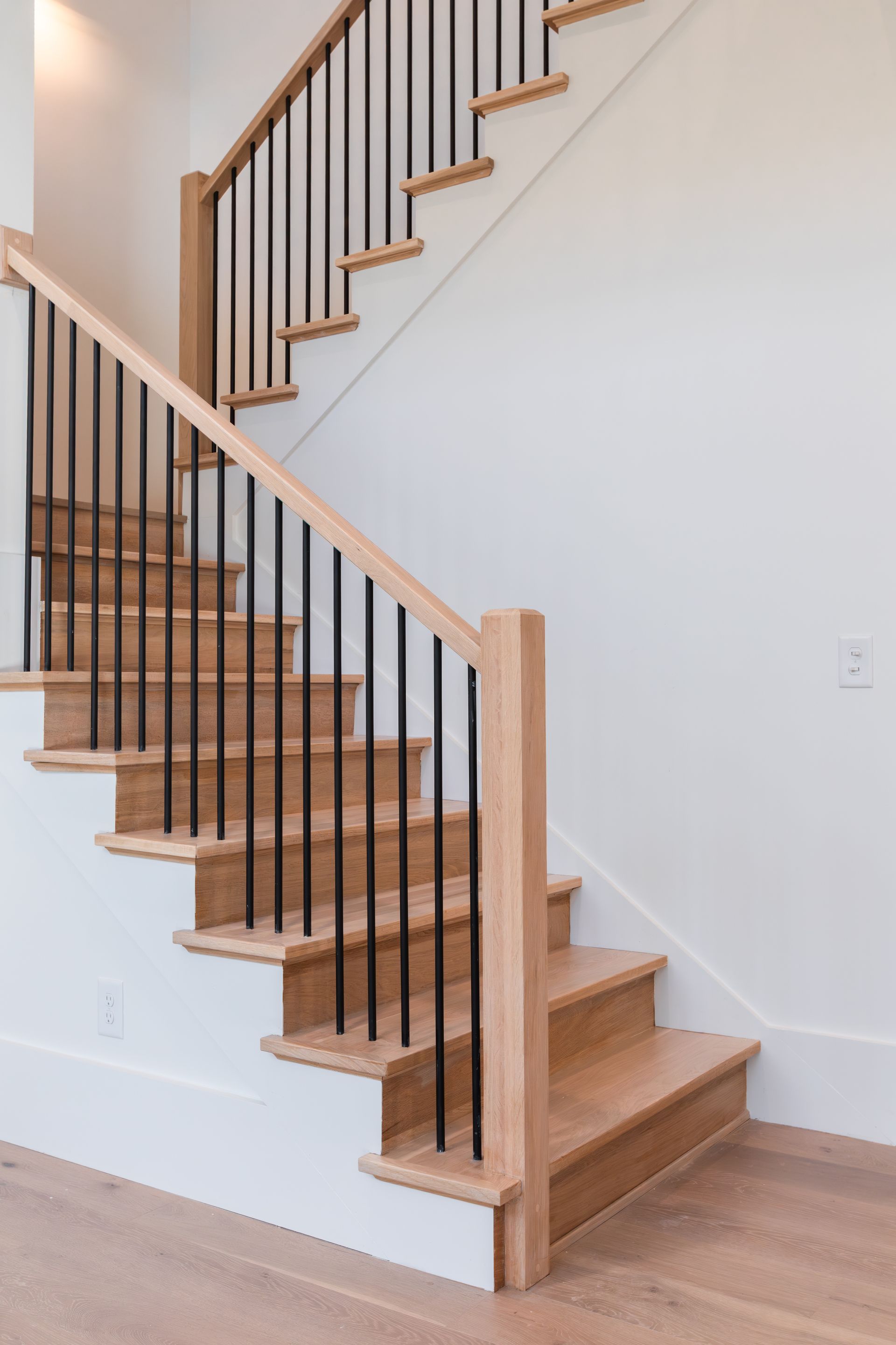 Wooden staircase with black metal railings against a white wall.