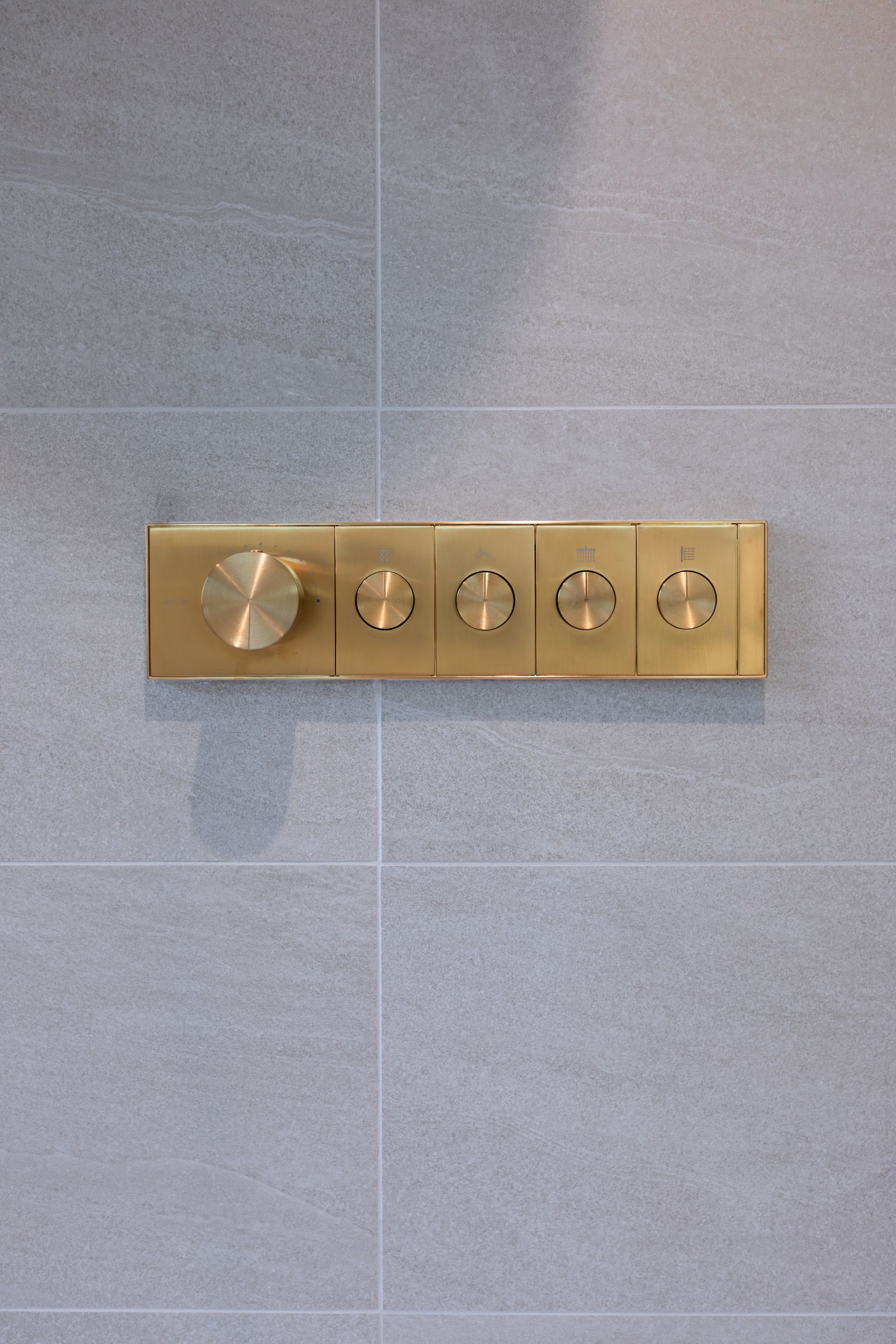 Brass shower controls on gray tiled wall.