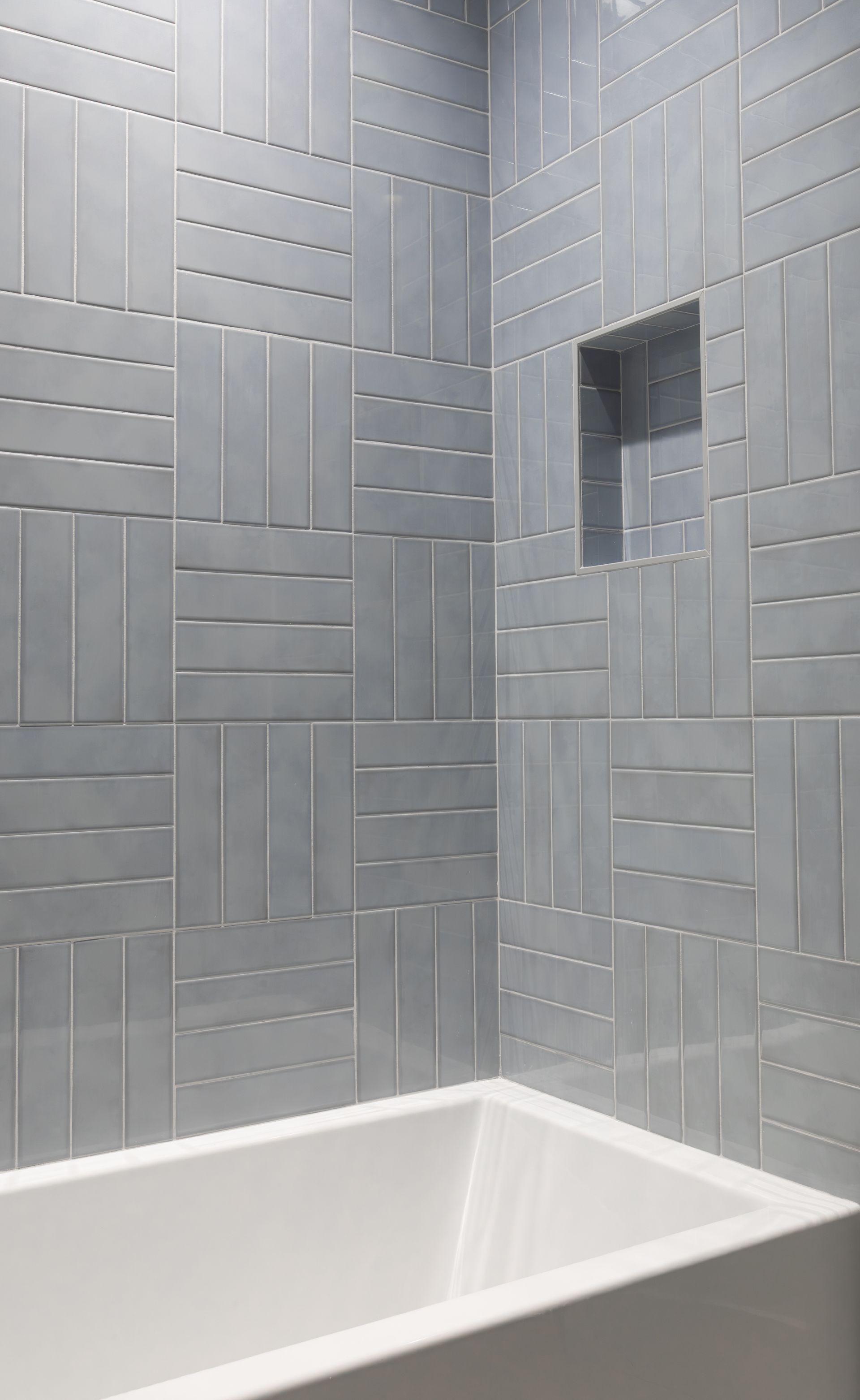 Gray tiled shower with inset shelf above a white bathtub.