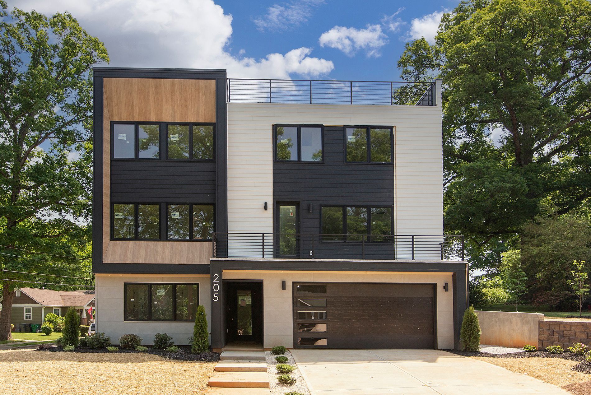 Modern three-story house with black and light wood accents, garage, and rooftop deck.