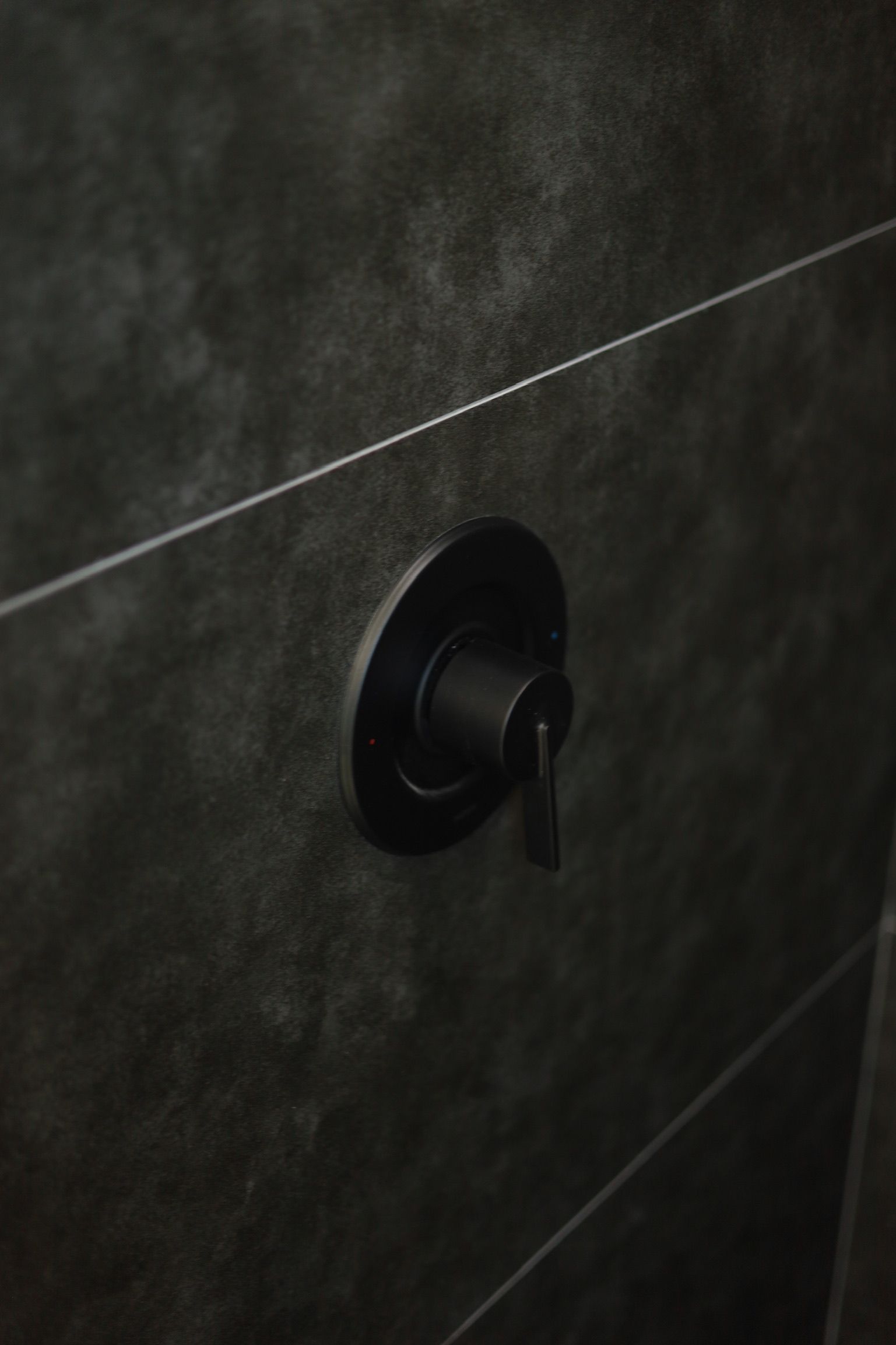 Black shower valve on dark gray tiled wall.