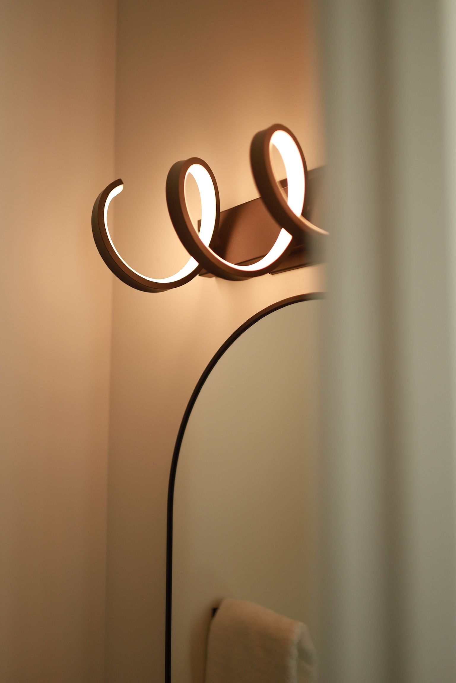 A modern, swirly light fixture above a bathroom mirror, with a towel below.