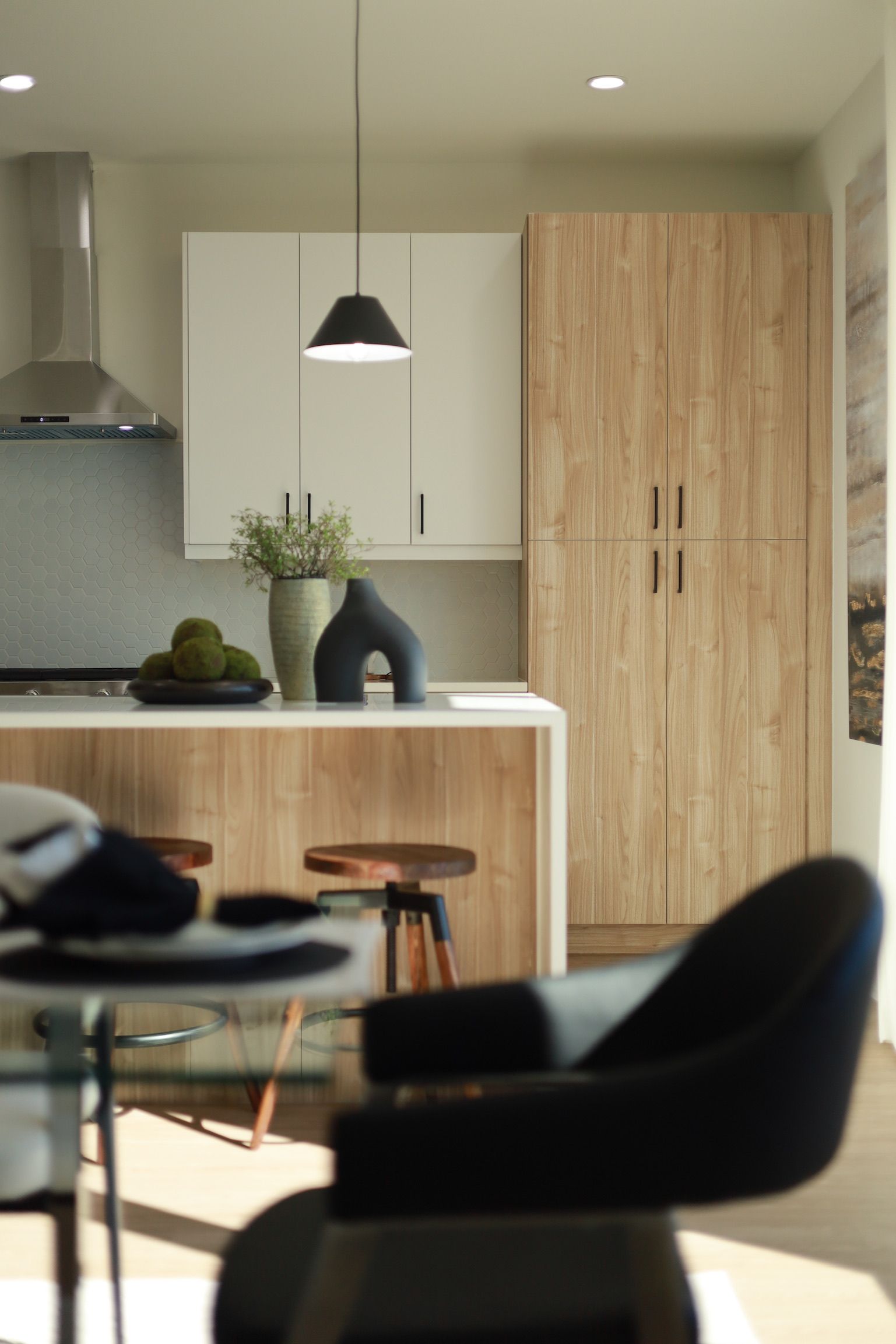 Kitchen with light wood cabinets, white counter, black pendant light, and a blue chair.