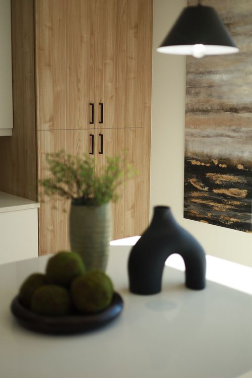 Kitchen island with decorative objects: green vase, moss balls, and black sculpture, with wood cabinets in the background.