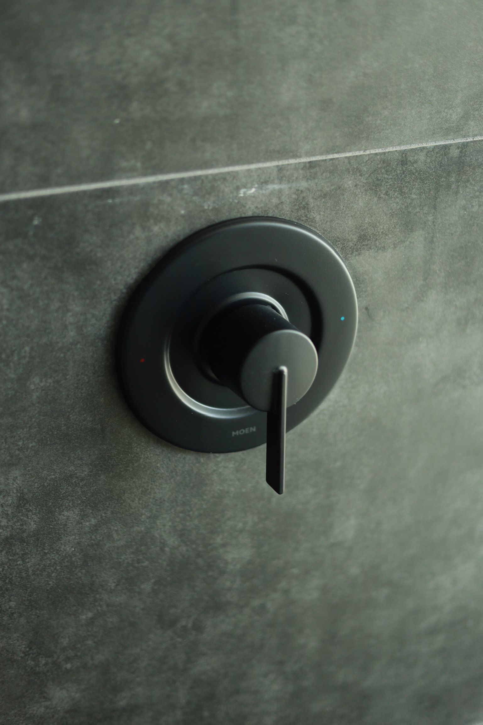 Black shower faucet on a dark grey tile wall with a single lever.