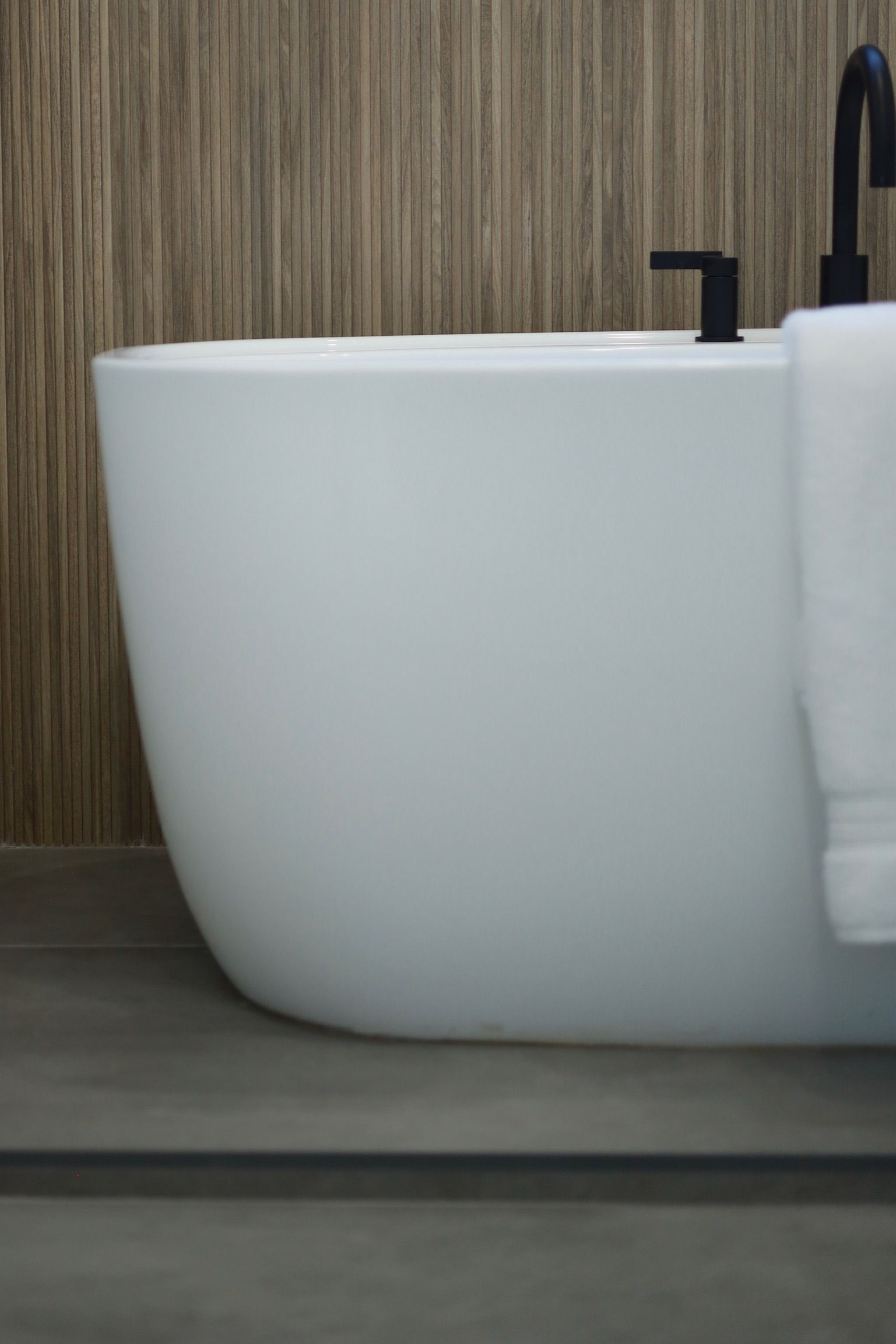 White bathtub with black fixtures against a wooden wall. A towel hangs on the side.