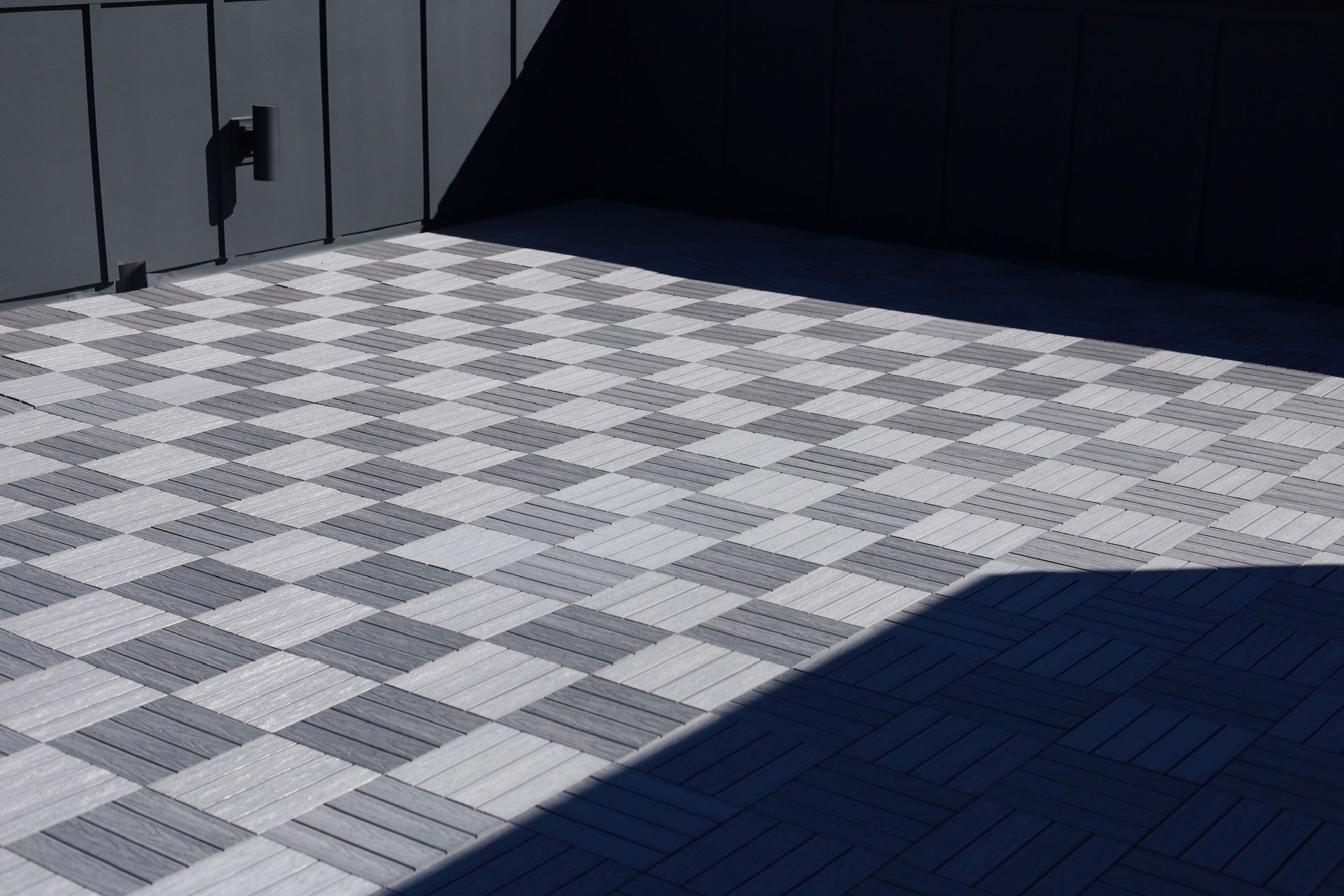 Checkerboard-patterned gray and white tiles on a deck or patio, with a wall and shadow.