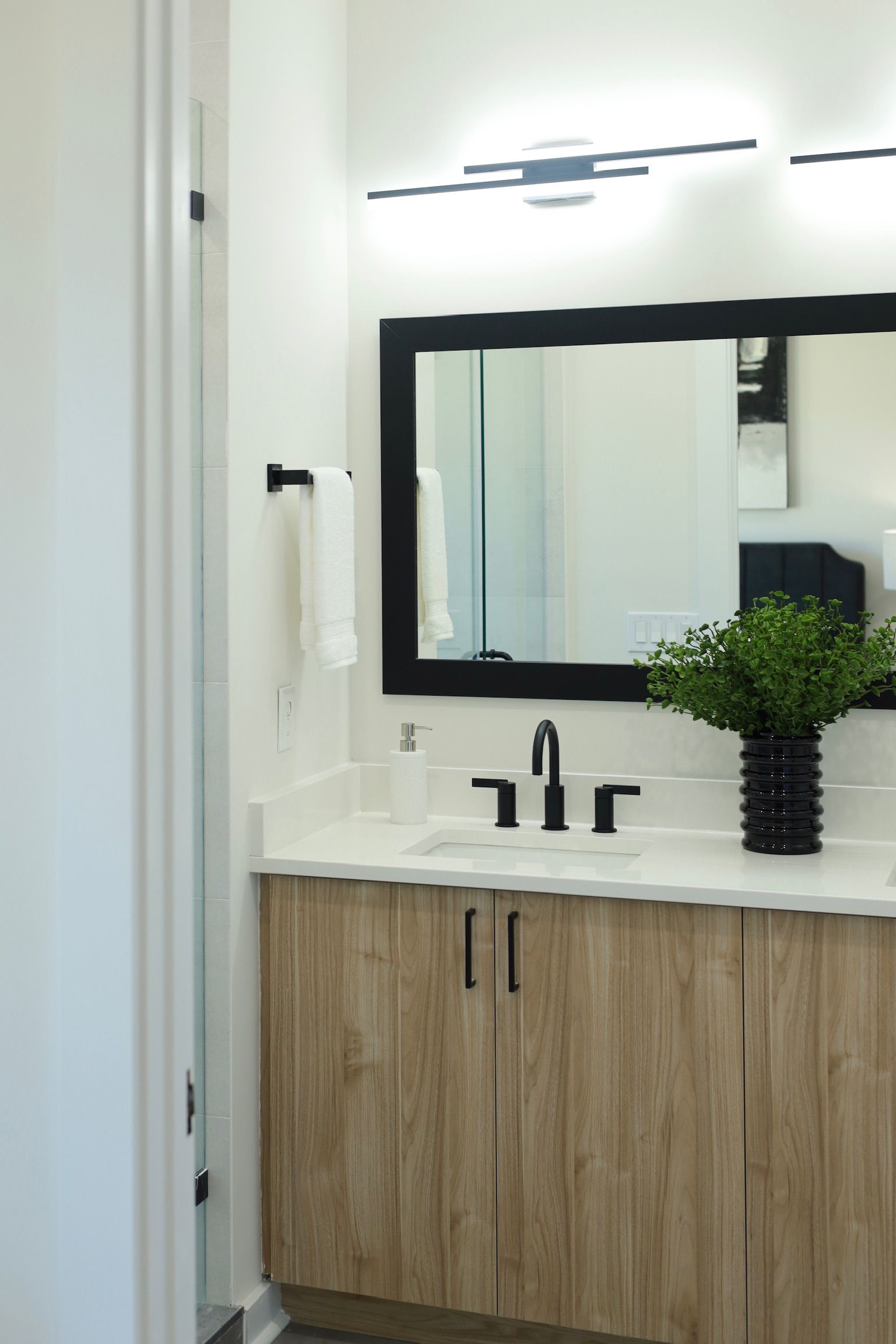 Bathroom with light wood vanity, black fixtures, and a mirror with black frame.