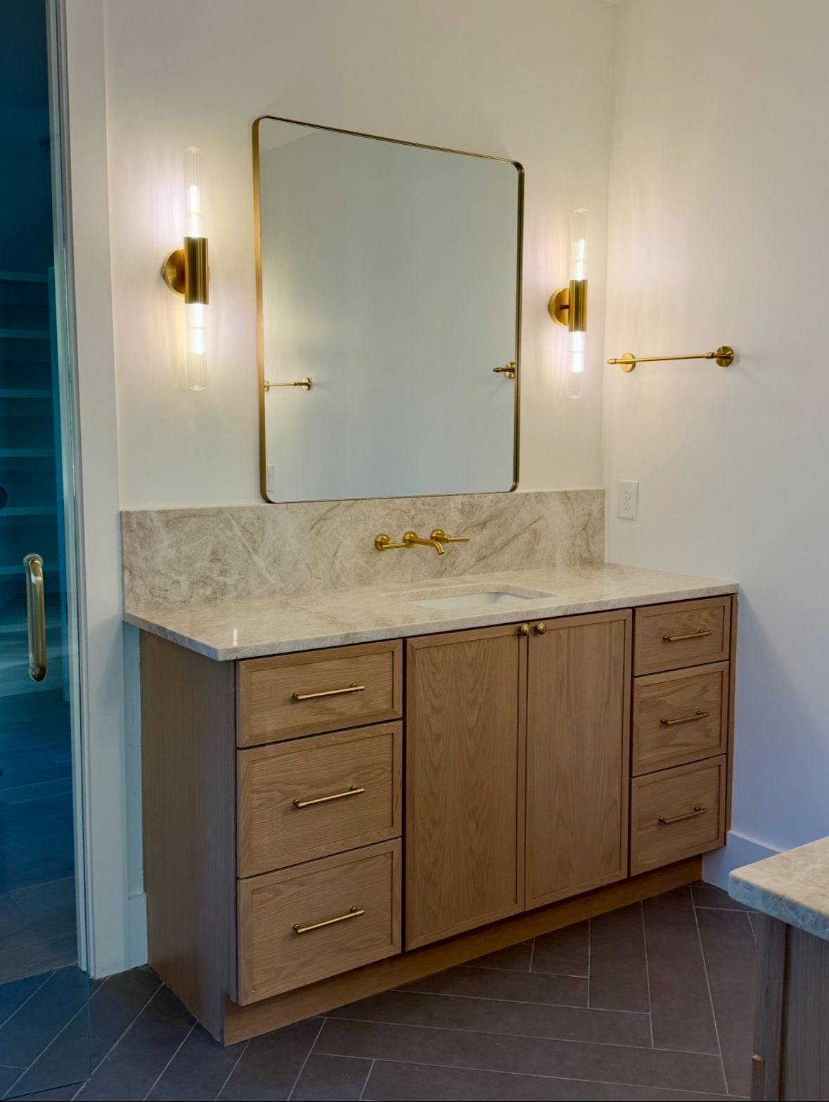 Bathroom vanity with gold fixtures, a large mirror, and light wood cabinetry.