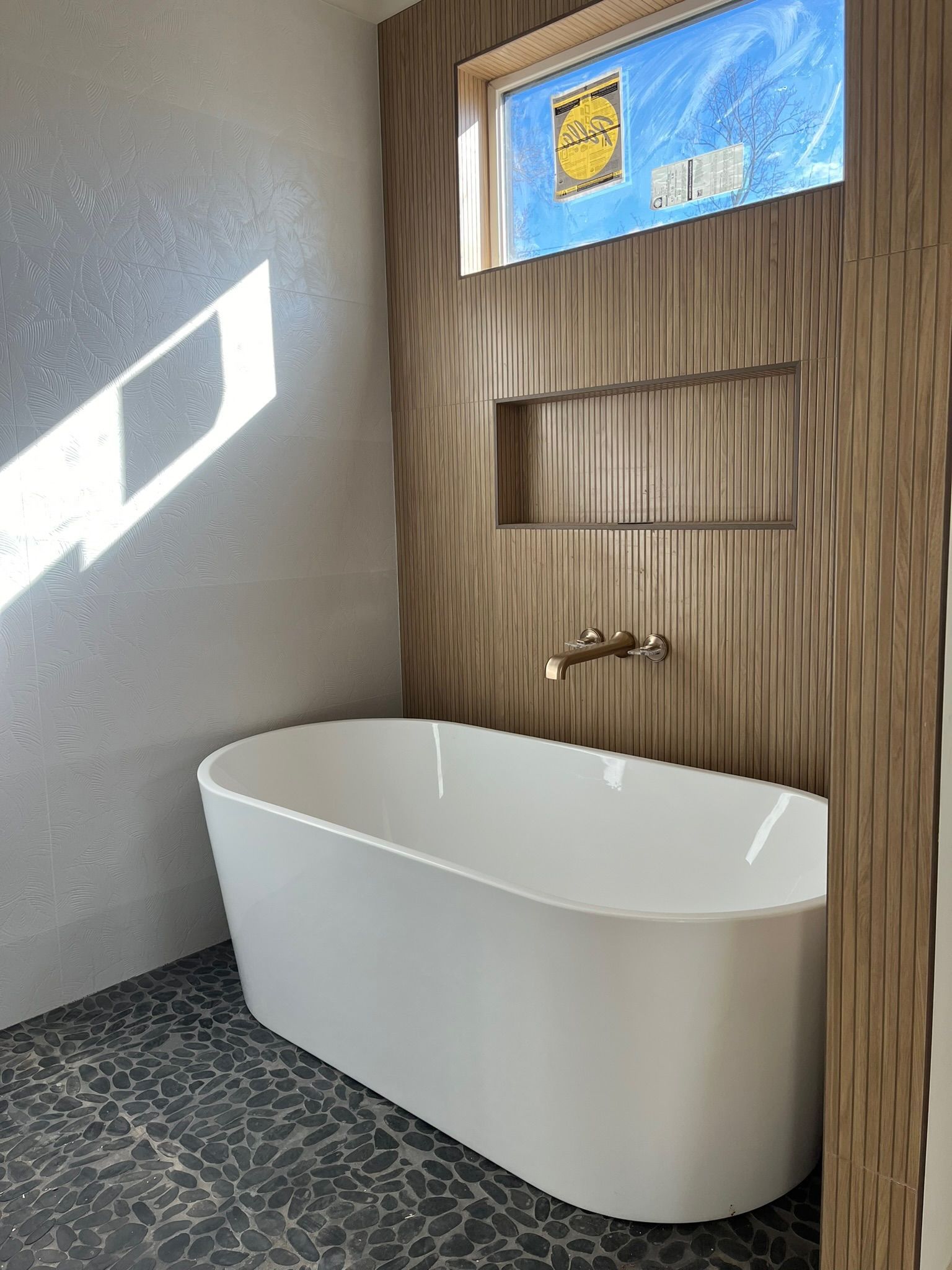 Modern bathroom with white freestanding tub, textured wood accent wall, and window.