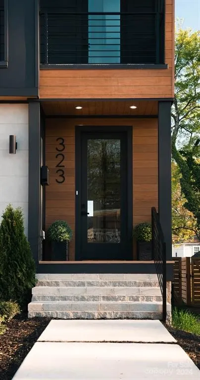 Modern house entrance with black door, wood siding, and stone steps. Black house number 