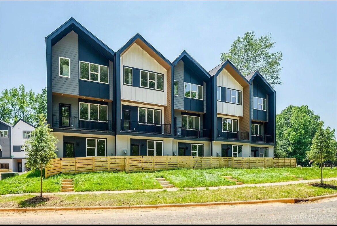Modern townhouses with black and white exteriors, set on a grassy hill.