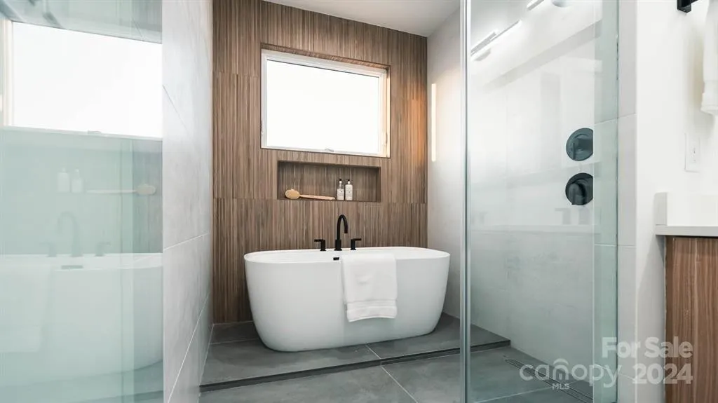 Modern bathroom with a freestanding tub, wood-paneled wall, and glass shower.