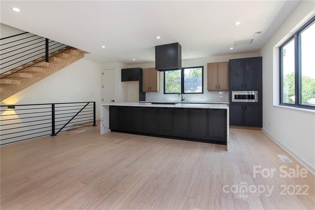 Modern kitchen with island, dark cabinets, light wood floors, and stairs.